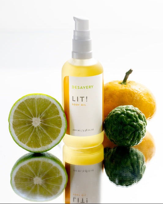 Bottle of Desavery LIT! body oil with citrus fruits on a white background