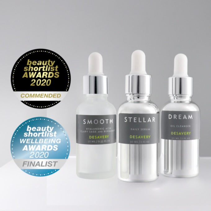 Two award medallions for Beauty Shortlist Awards. Three skincare products in 30 ml glass bottles. Smooth Hyaluronic Acid in a frosted glass bottle with white pipette, Stellar Daily Serum in a silver 30 ml bottle and white pipette, Dream Oil Cleanser in a silver bottle with white pipette.
